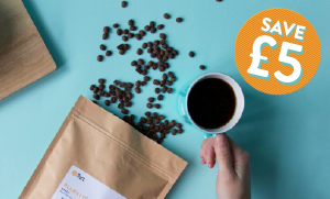 Pact coffee beans spilling out of bag with cup of coffee